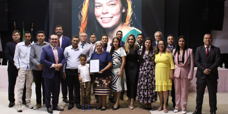 Autoridades, familiares e convidados posam em cerimônia na Câmara de Itararé em homenagem a Raquel de Oliveira Lima, com imagem da homenageada projetada ao fundo.