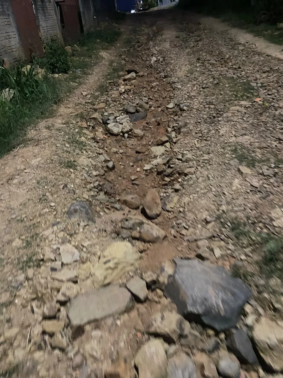 Pedras soltas e sulcos em rua de terra junto a residências no registro de Pedra Branca