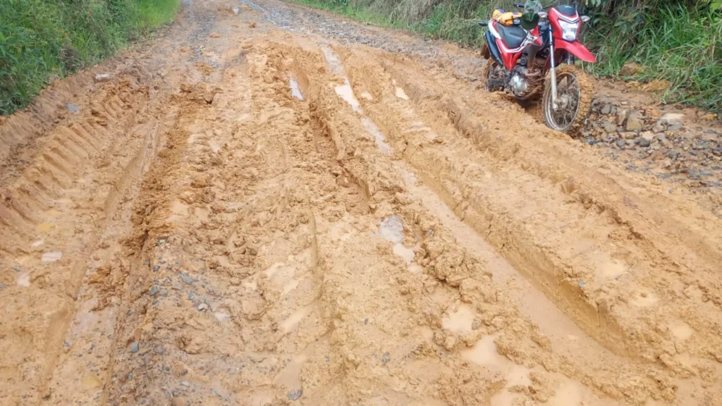 Motocicleta vermelha junto a sulcos e lama em uma estrada rural.