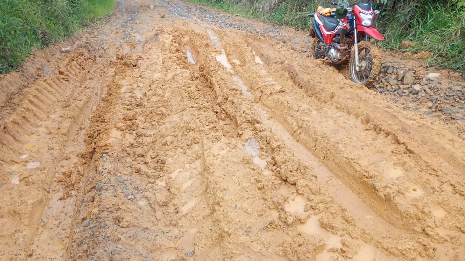 Estrada rural com lama, sulcos e uma motocicleta vermelha em Itararé, São Paulo