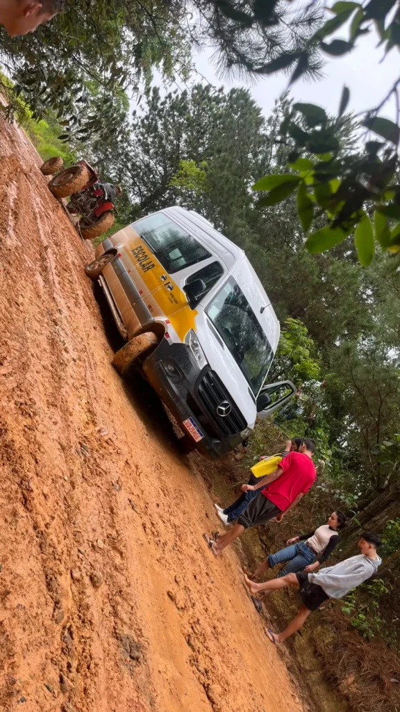 Van branca e amarela parada em uma estrada de terra, com pessoas ao lado.
