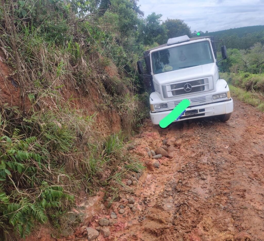 Caminhão branco em trecho estreito de estrada de terra com lama e sulcos.