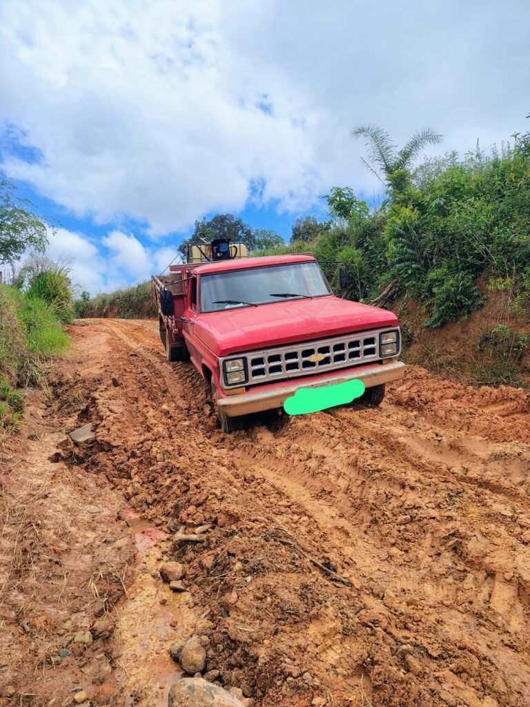 Caminhão vermelho sobre trecho de terra com lama e marcas profundas de pneus.